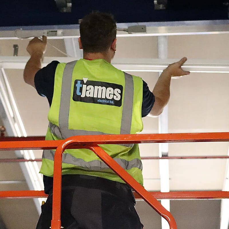 Electrician installing ceiling lights on scaffolding.